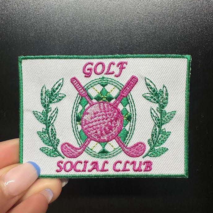 Embroidered patch with 'Golf Social Club' design held against a dark background
